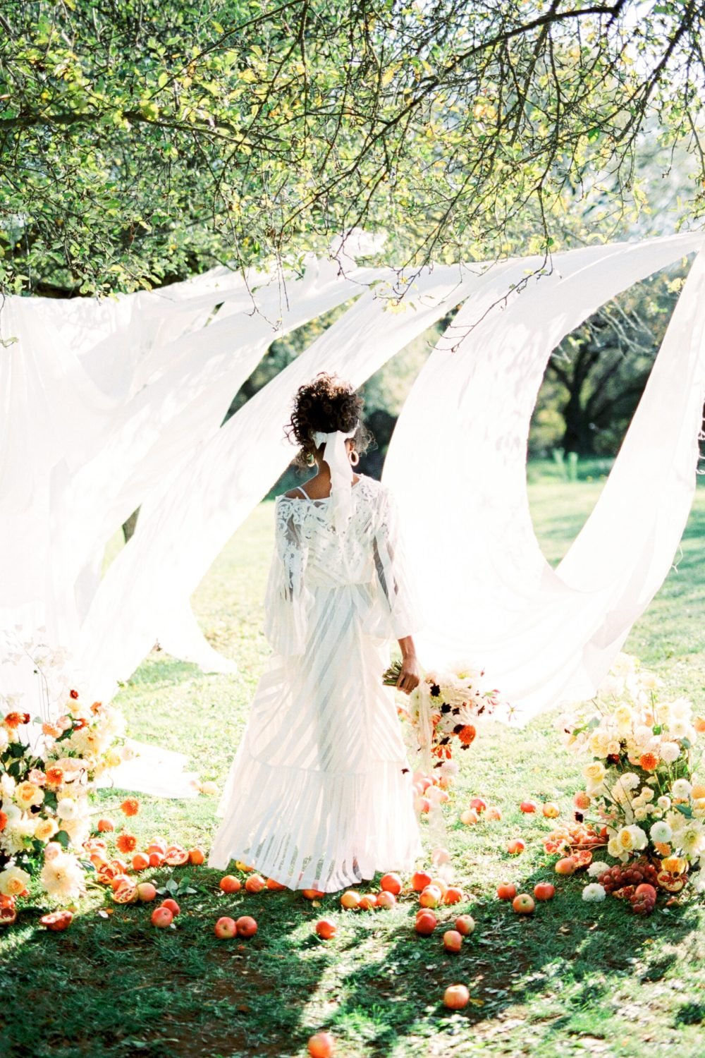 Woman with a bouquet of flowers stands in front of white curtains in the garden. Back view. High quality photo